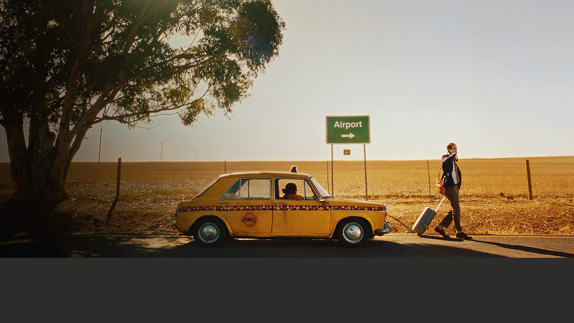 En gul taxi står på en landsväg. En man med en resväska går bort från taxin.