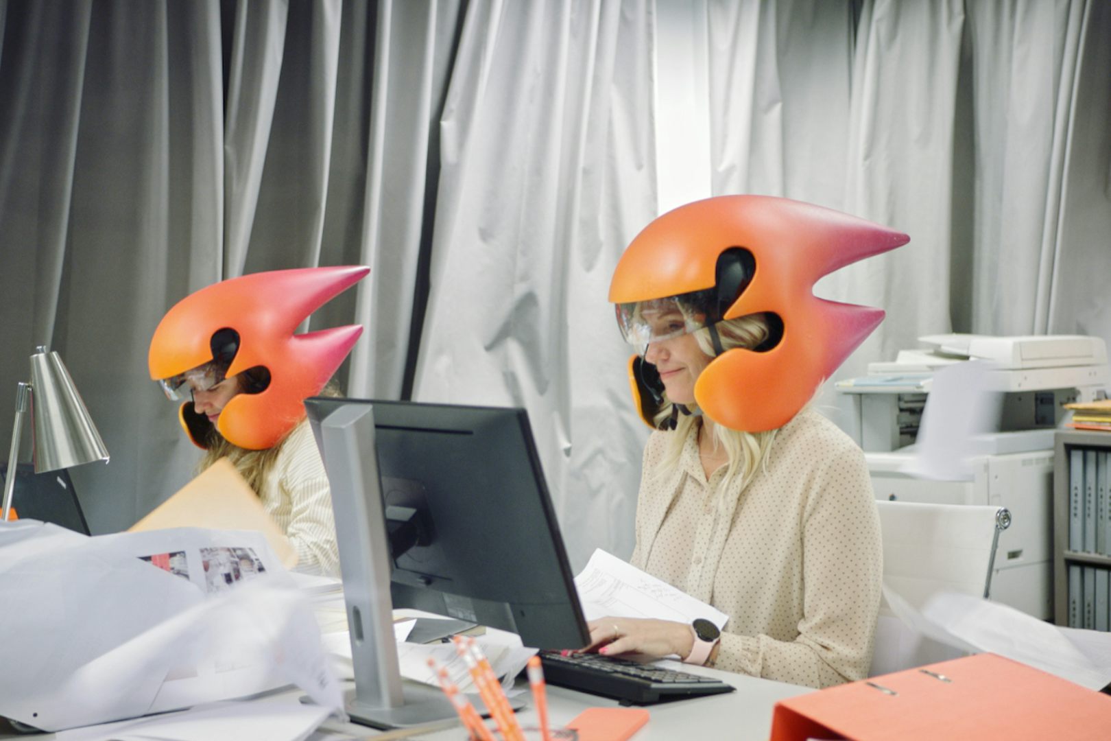 Två kvinnor sitter med hjälmar som är formade som treor och arbetar på ett kontor