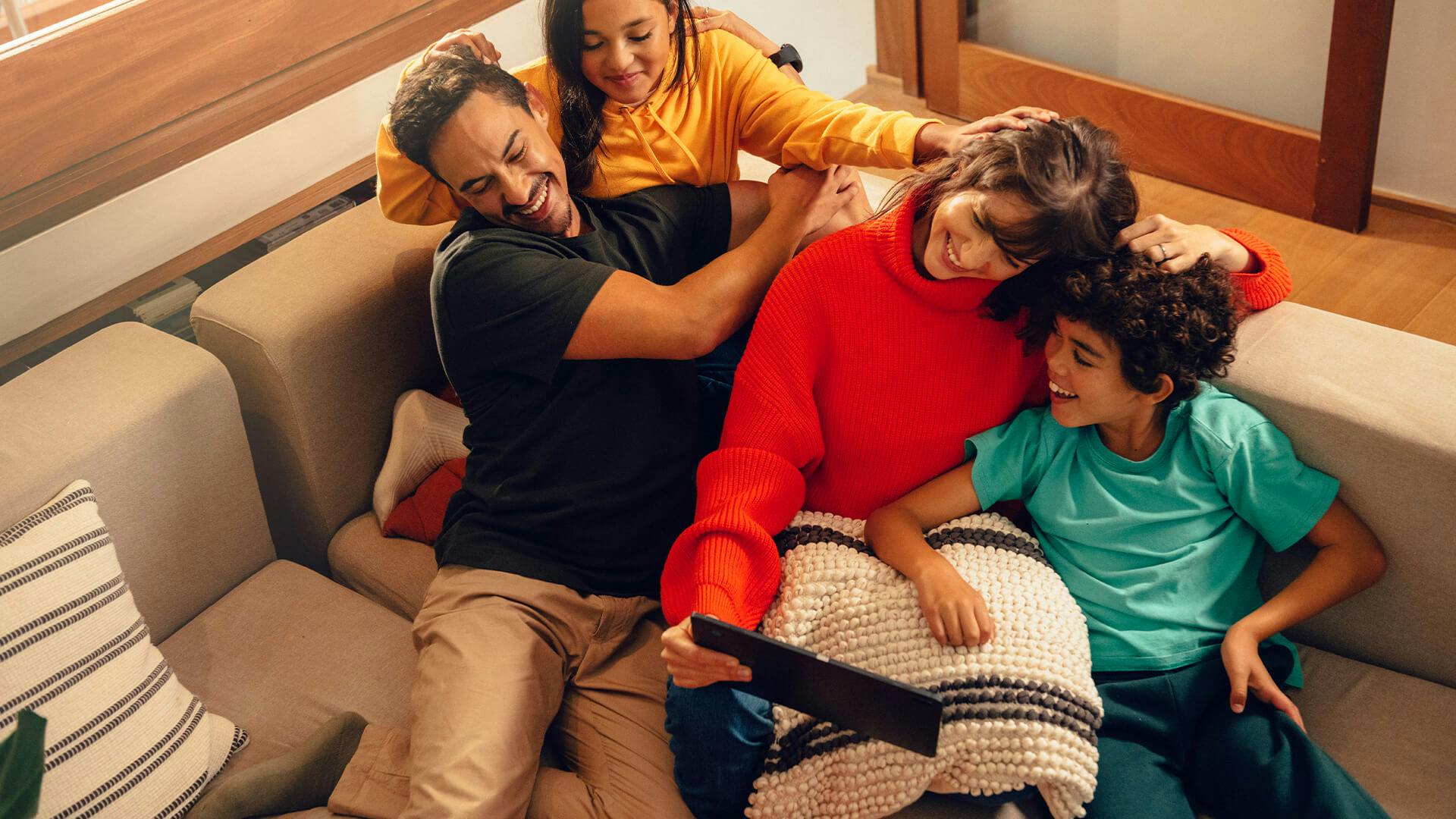 Familj i soffa tittar på surfplatta och ser glada ut.