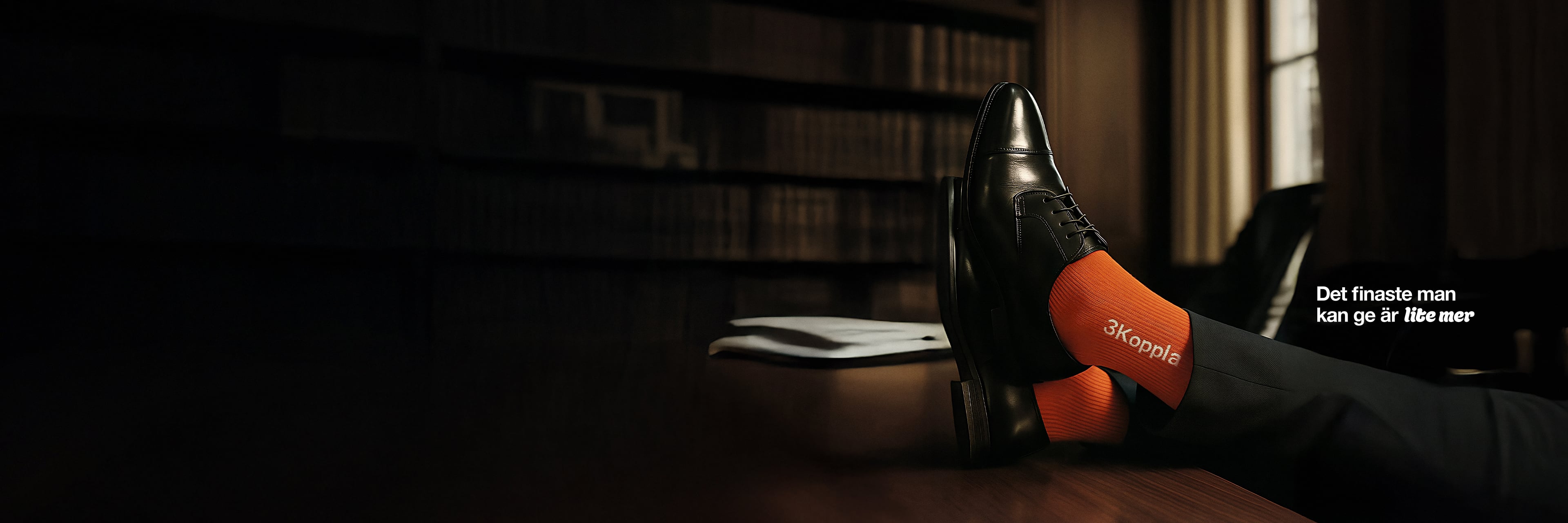 En person med svarta skor och orange strumpor vilar fötterna på ett bord i ett bibliotek. På de orange strumporna är det en 3Koppla logga i vitt. Texten: "Det finaste man kan ge är lite mer" står under fötterna.