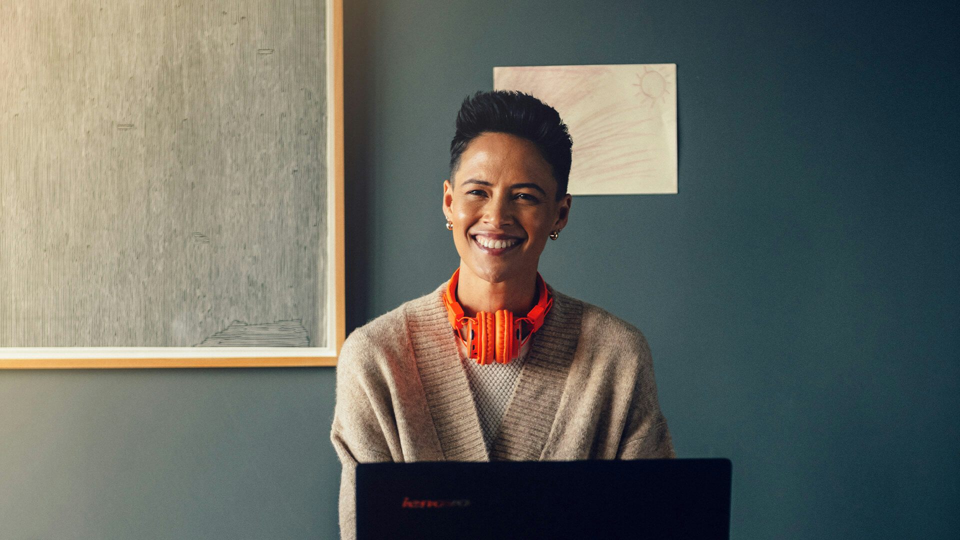En kvinna med orangea hörlurar sitter vid ett skrivbord och jobbar på en dator.